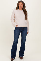 woman wearing a light pink cable-knit maternity sweater and dark blue flare jeans, posing with one hand in her pocket