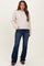 woman wearing a light pink cable-knit maternity sweater and dark blue flare jeans, posing with one hand in her pocket