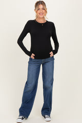 woman wearing a black long sleeve maternity top and loose blue jeans, smiling with hands in pockets