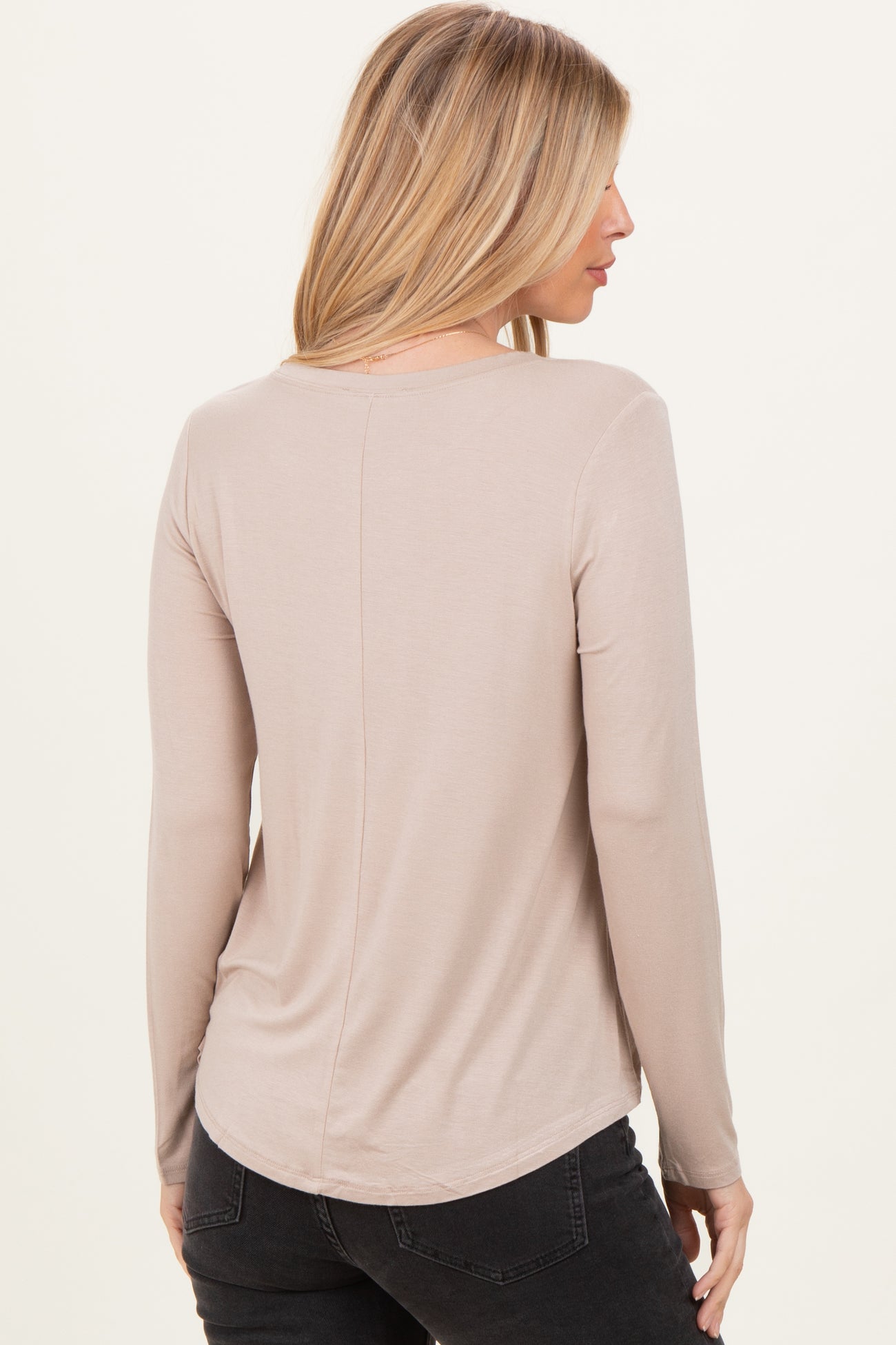 woman wearing a beige long sleeve top with a rounded hem and a relaxed fit, viewed from the back