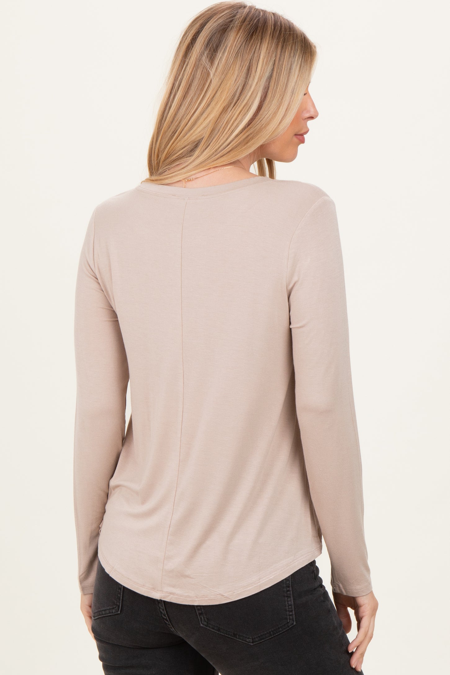 woman wearing a beige long sleeve top with a rounded hem and a relaxed fit, viewed from the back