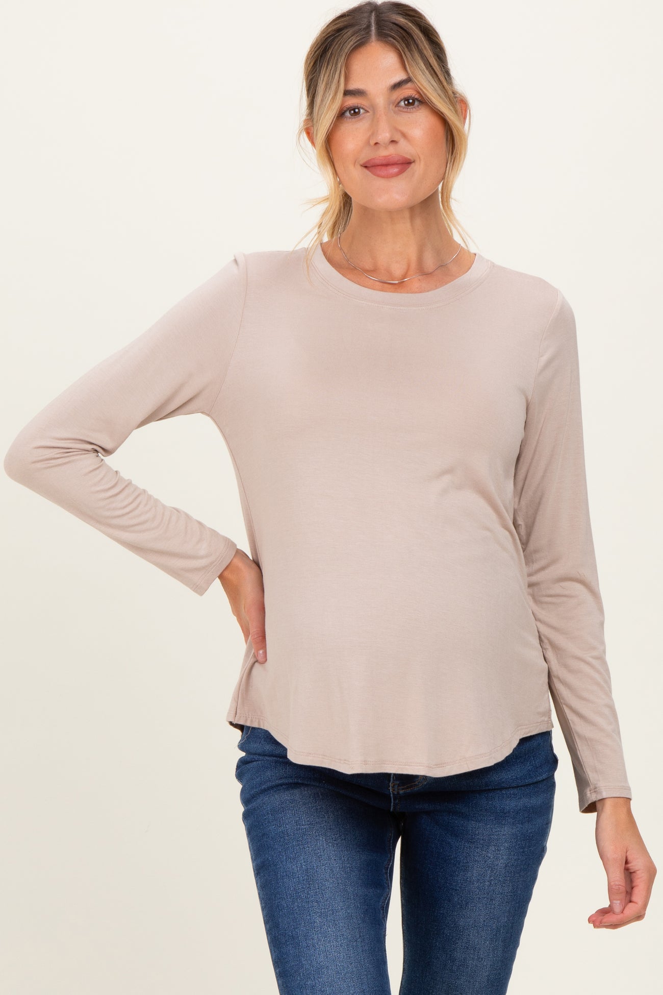woman wearing a light beige long sleeve maternity top and showing her baby bump while posing
