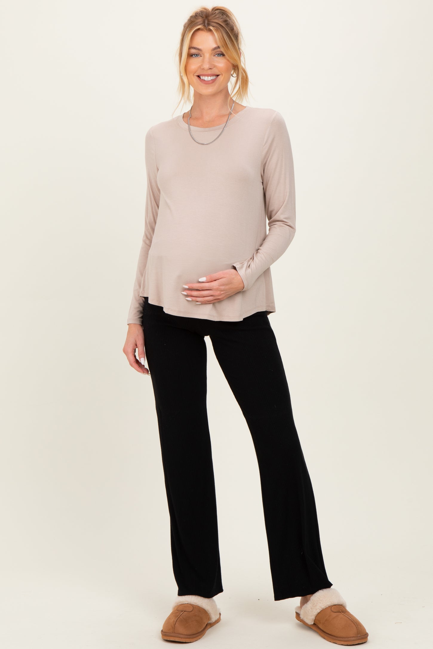 woman wearing a beige long sleeve maternity top and black pants, showing her baby bump, paired with cozy slippers