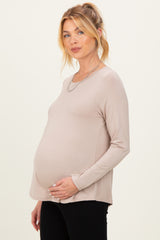 woman wearing a beige long sleeve maternity top and holding her baby bump