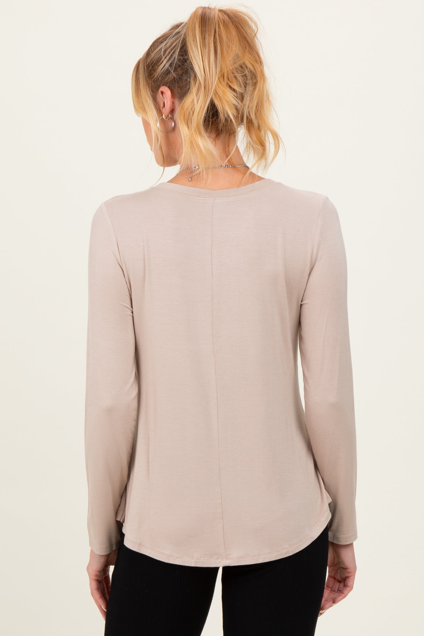 woman wearing a light beige maternity long sleeve top, showing the back view with a curved hemline