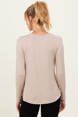 woman wearing a light beige maternity long sleeve top, showing the back view with a curved hemline