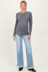 woman wearing a dark grey long sleeve maternity top and light blue flared jeans, showing her baby bump