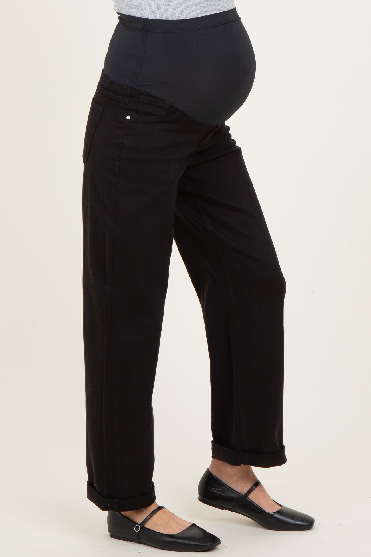 woman wearing black maternity jeans with a high waistband and rolled cuffs, revealing a baby bump