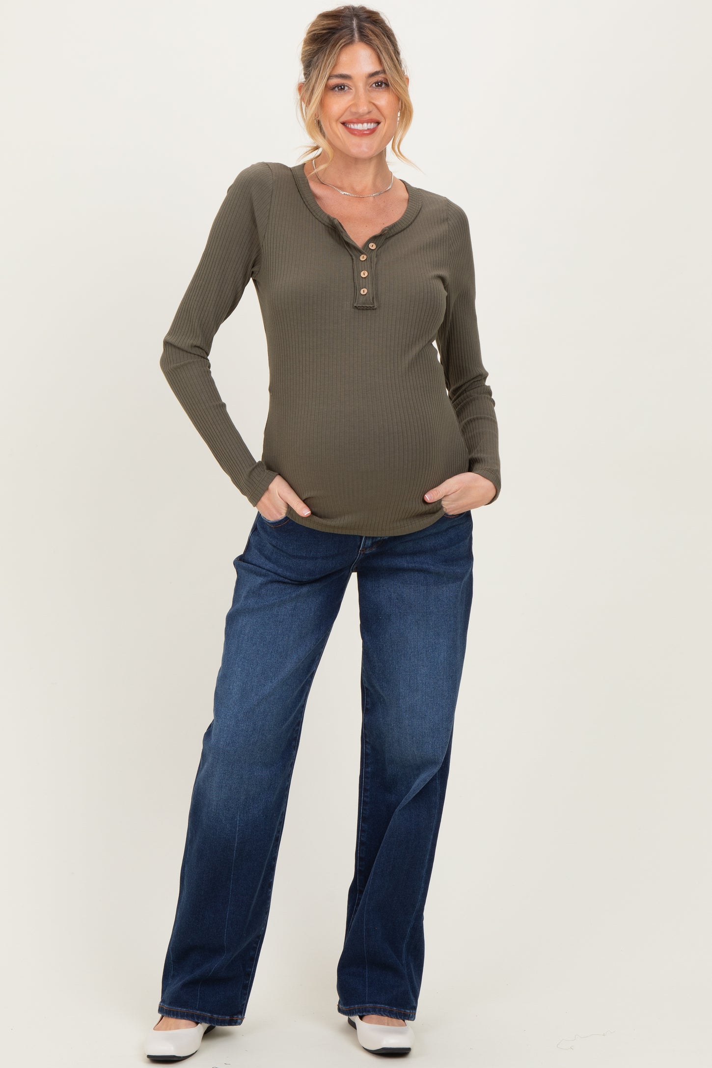 woman wearing an olive green maternity long sleeve henley top and blue jeans, showing her baby bump