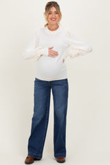 woman wearing a cream maternity sweater with puff sleeves and holding her baby bump, paired with wide-leg jeans
