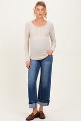 woman wearing a beige scoop neck maternity top and blue wide-leg jeans, showcasing her baby bump