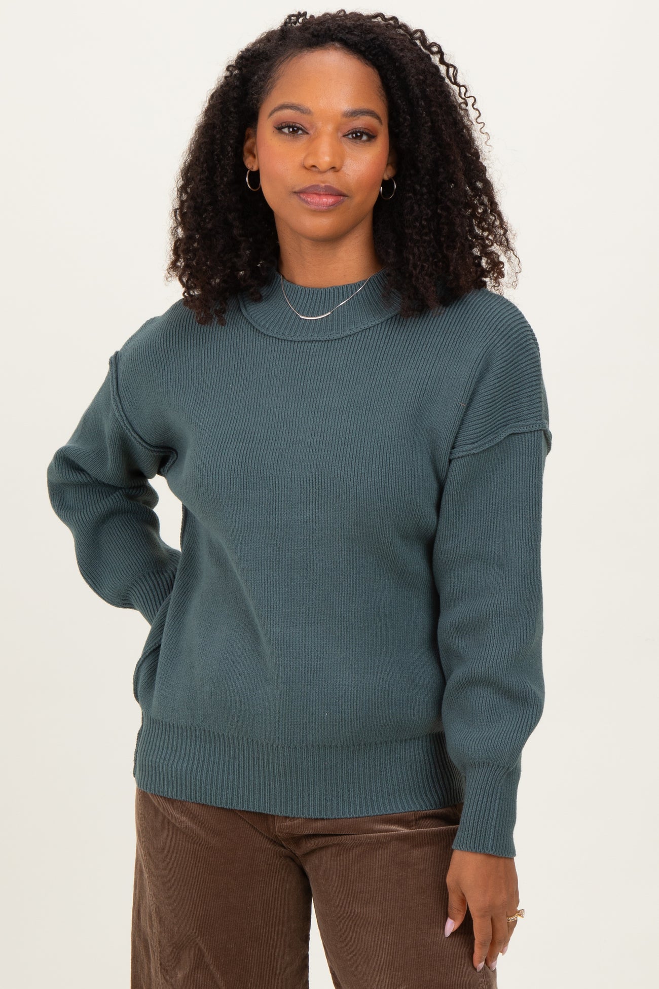 woman wearing a dark teal knitted sweater with a relaxed fit and ribbed details paired with brown corduroy pants