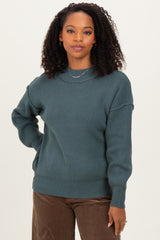 woman wearing a dark teal knitted sweater with a relaxed fit and ribbed details paired with brown corduroy pants