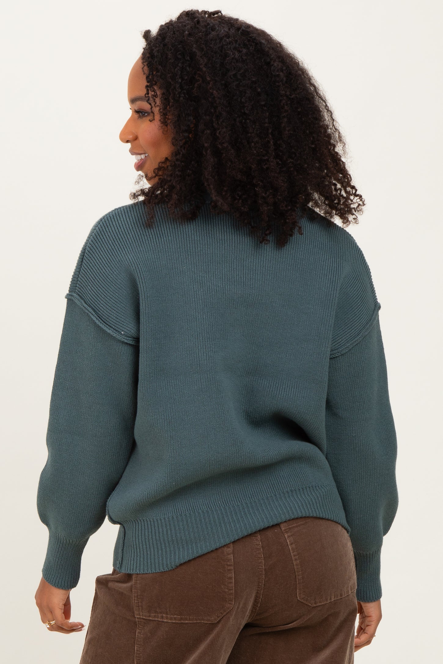 woman wearing a teal oversized sweater with ribbed details, styled with brown corduroy pants
