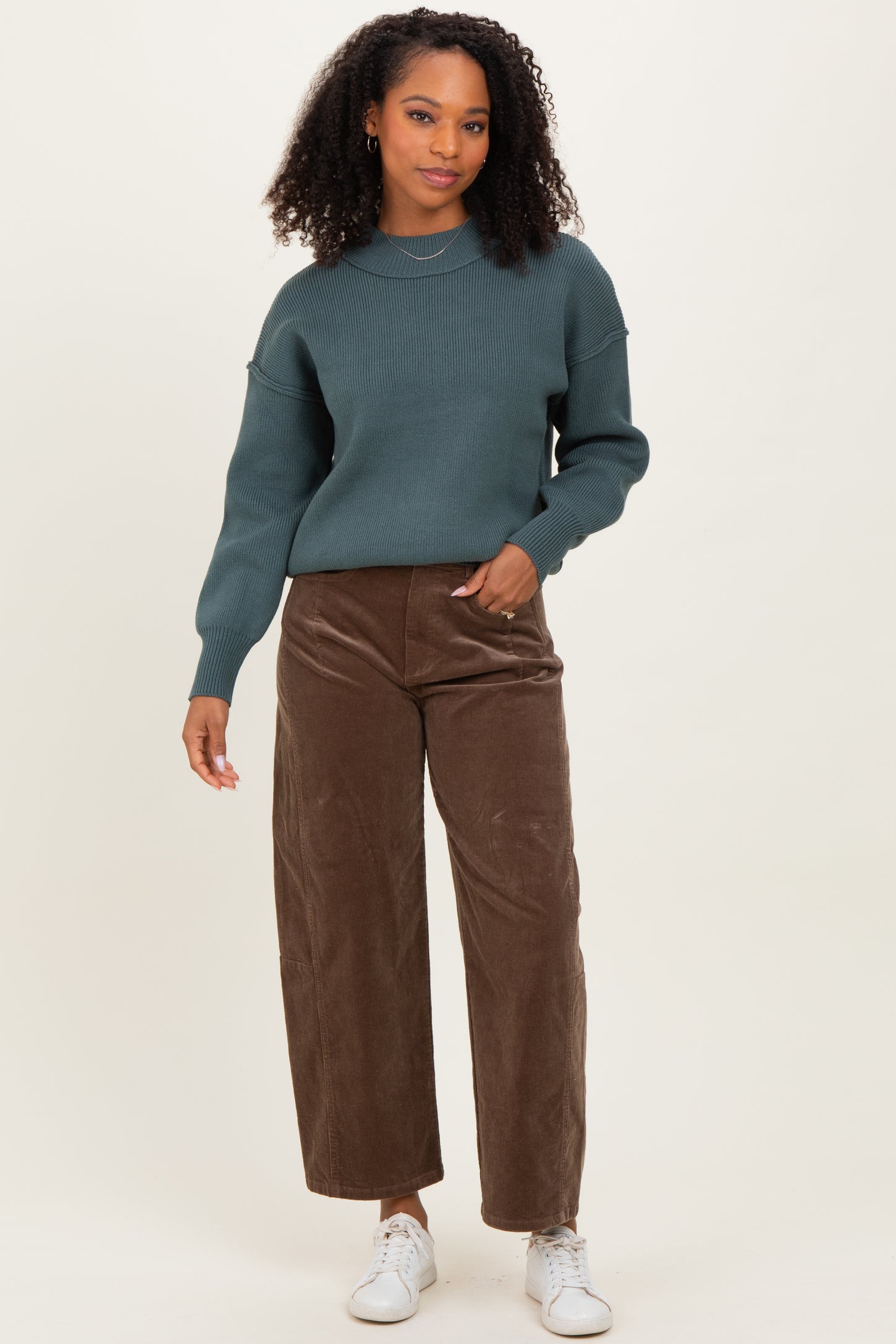 woman wearing a dark teal knitted sweater and brown wide-leg corduroy pants with white sneakers