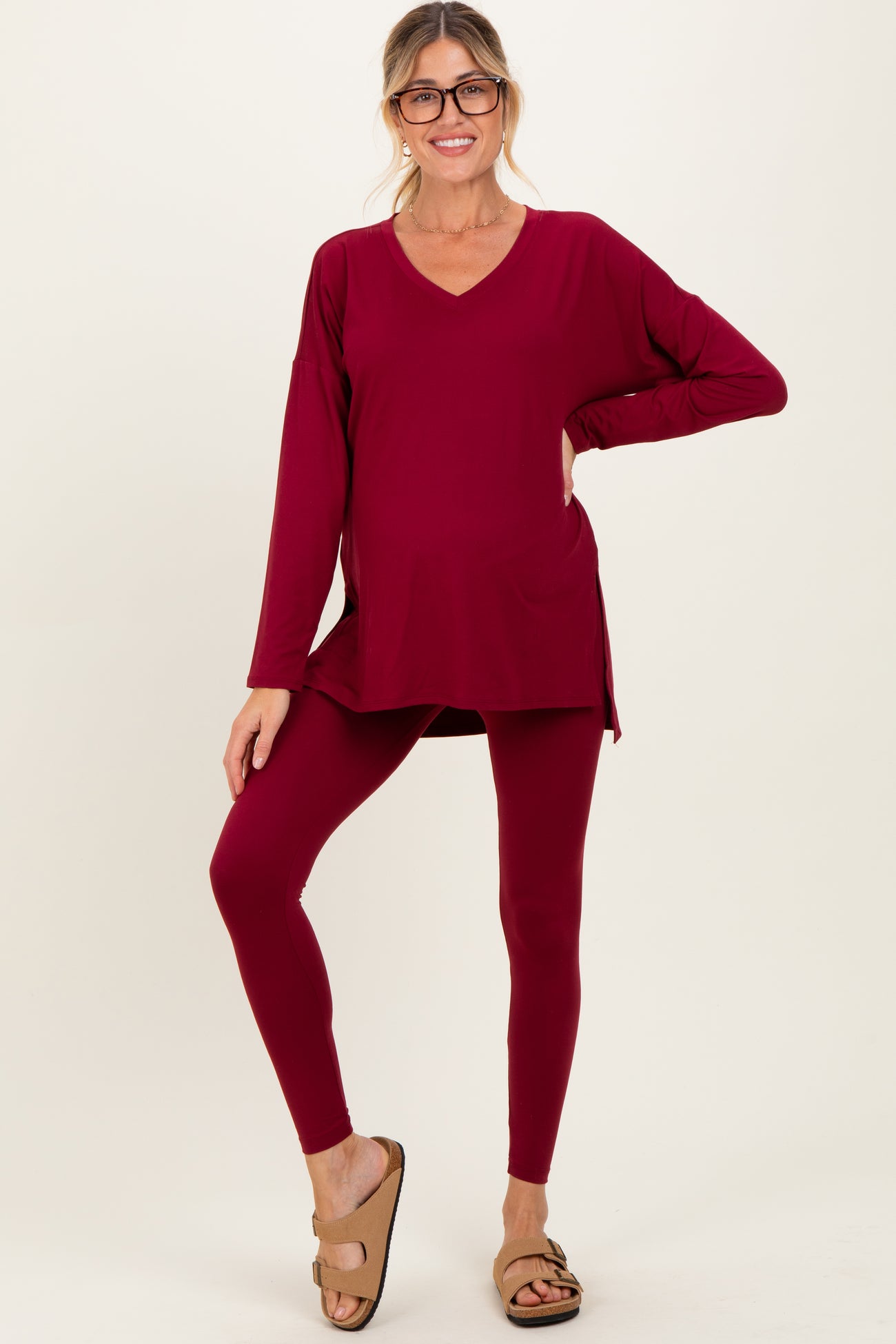 woman wearing a burgundy maternity top with a v-neck and long sleeves paired with matching leggings and sandals, baby bump visible