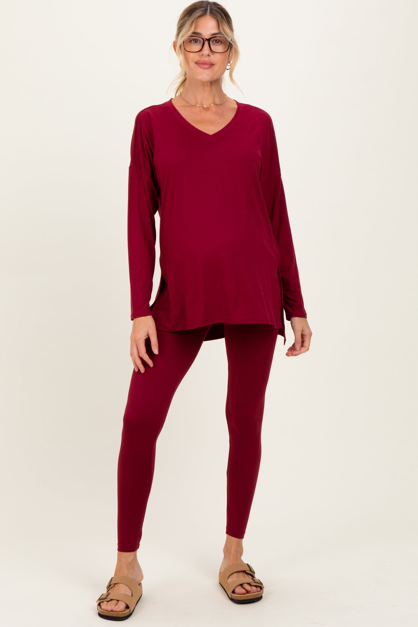 woman wearing a burgundy long sleeve maternity tunic top and matching leggings, showing her baby bump