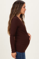 woman wearing a dark brown long sleeve maternity top and holding her baby bump