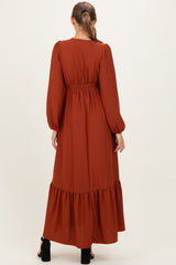 woman wearing a rust-colored long sleeve maternity maxi dress with an elastic waist and tiered hemline