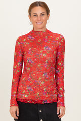 woman wearing a red long sleeve top with floral print and a high neckline, standing against a plain background