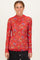 woman wearing a red long sleeve top with floral print and a high neckline, standing against a plain background