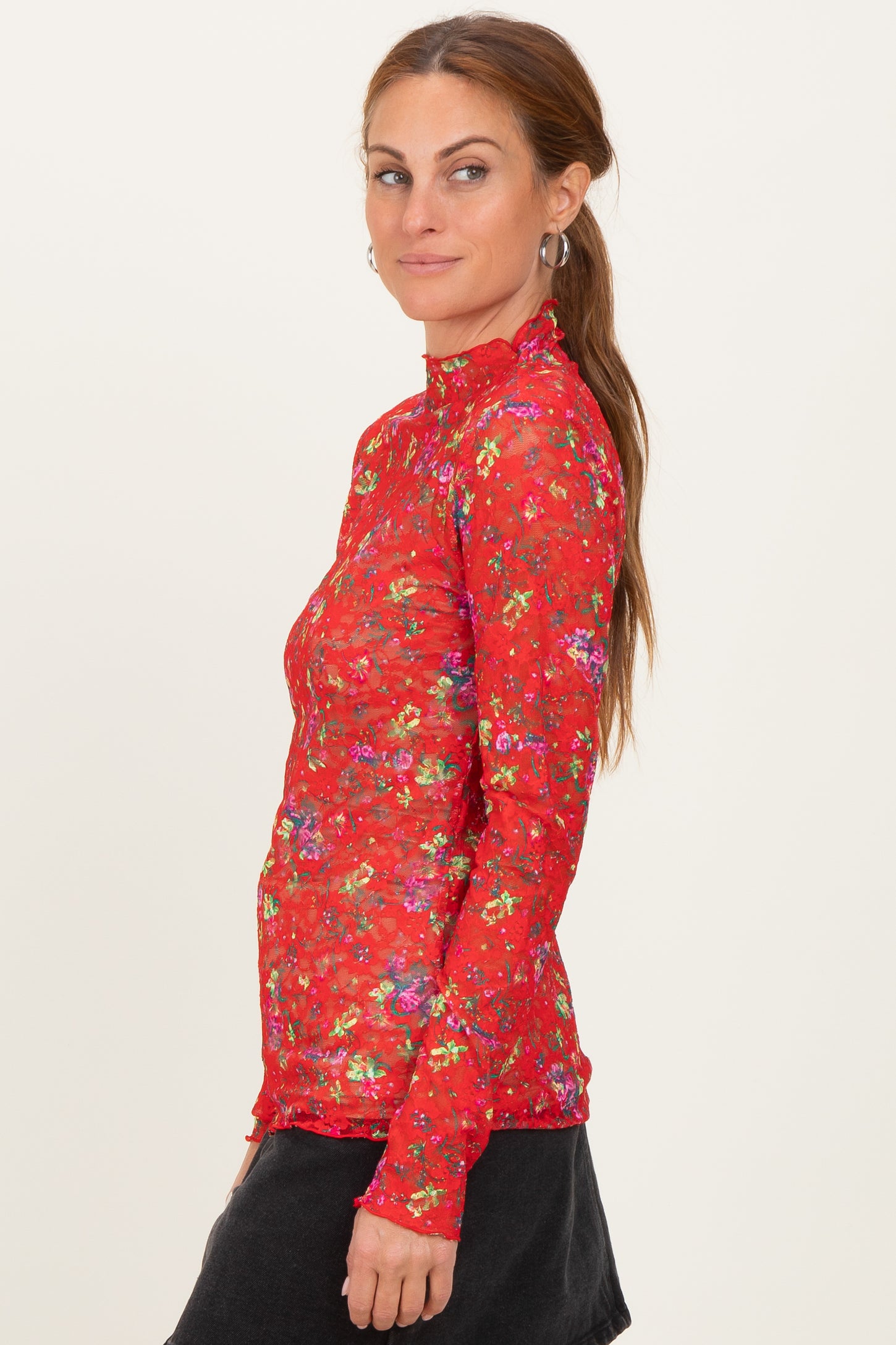woman wearing a red long sleeve top with a floral print and high neckline, styled with a black skirt