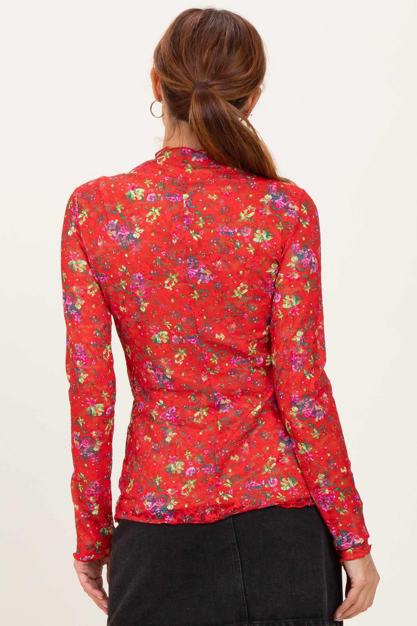 woman wearing a red long sleeve floral top, view from the back with colorful floral patterns