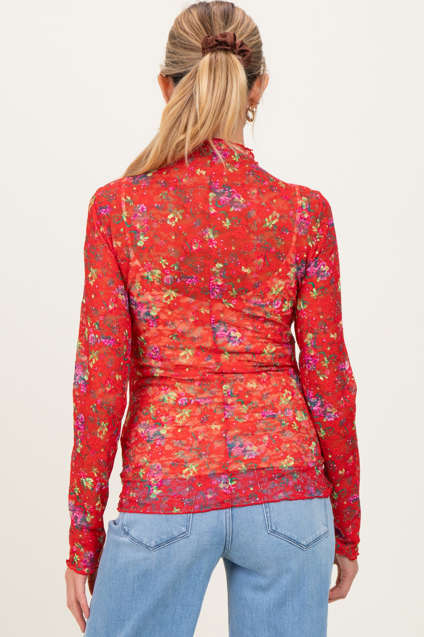 woman wearing a red floral maternity top with long sleeves, viewed from the back, paired with blue jeans