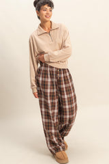 woman wearing a beige zip-up pullover and brown plaid wide-leg pants with buttons, posing in a relaxed manner