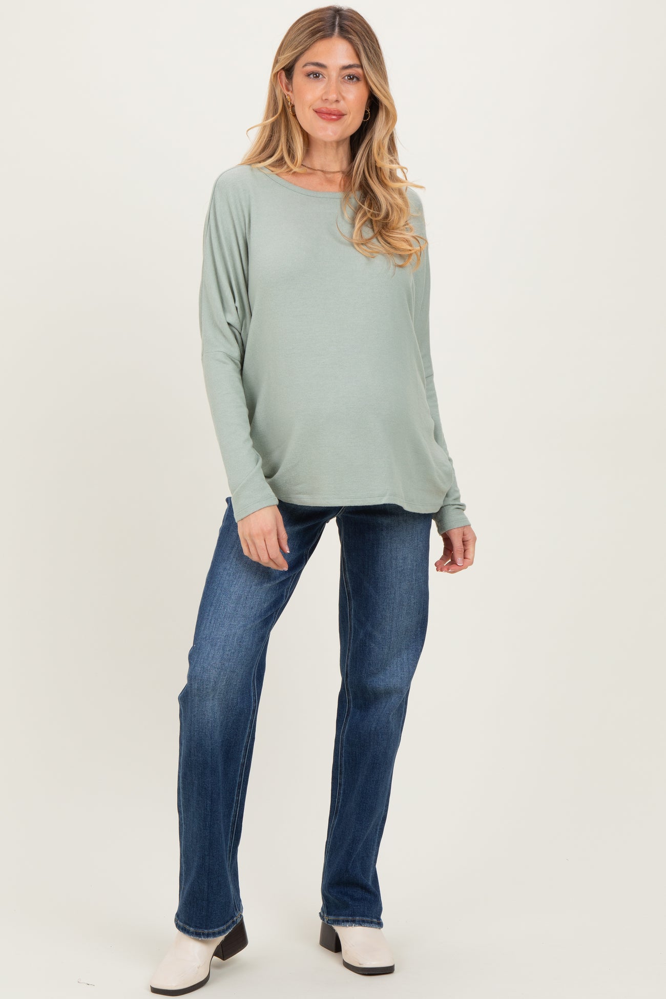woman wearing a light green long sleeve maternity top and blue jeans, with a visible baby bump