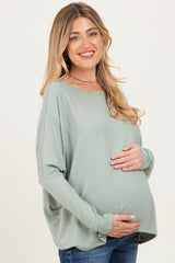 woman wearing a light green long sleeve maternity top and holding her baby bump