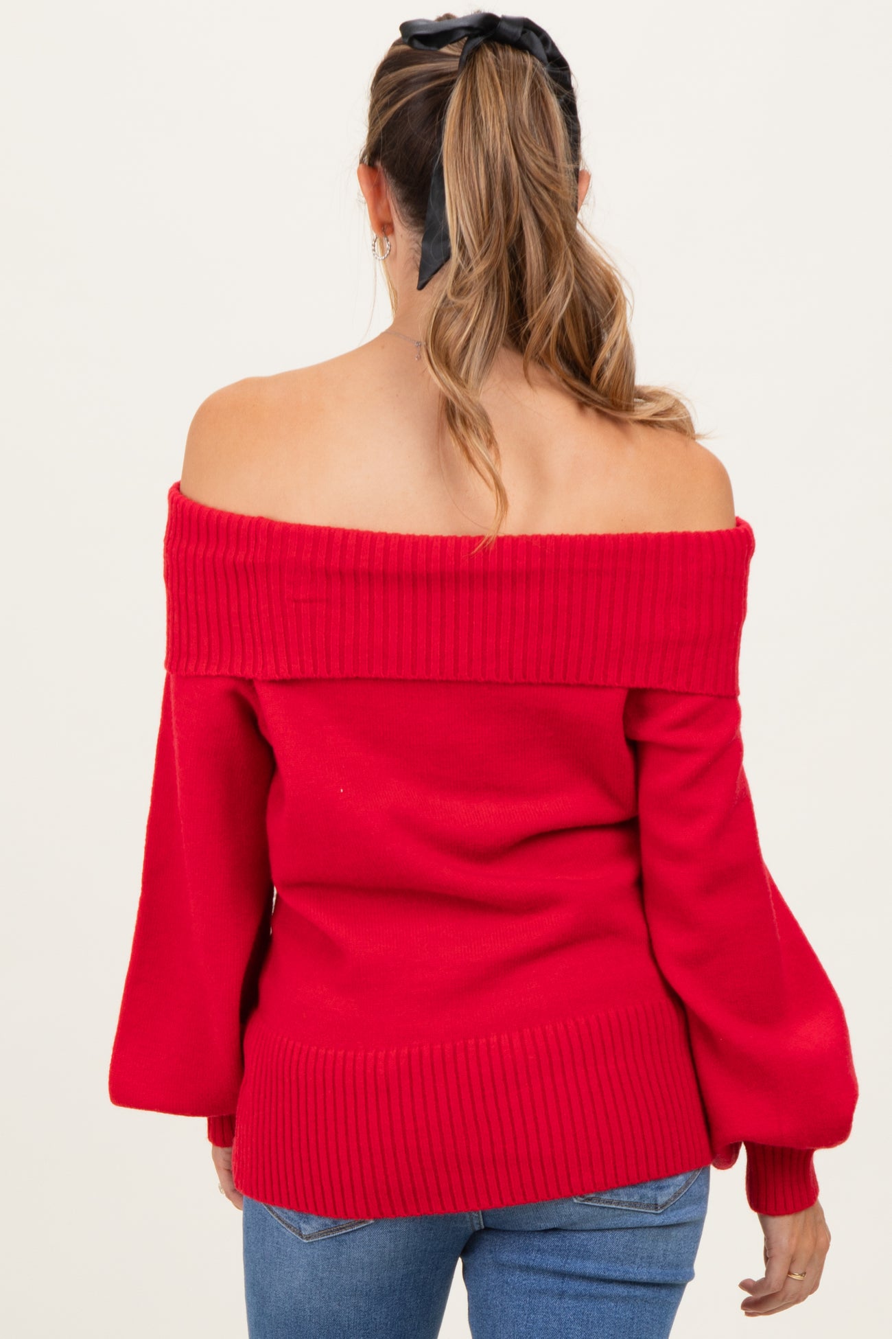 woman wearing a red off-the-shoulder maternity sweater with ribbed detailing and bell sleeves