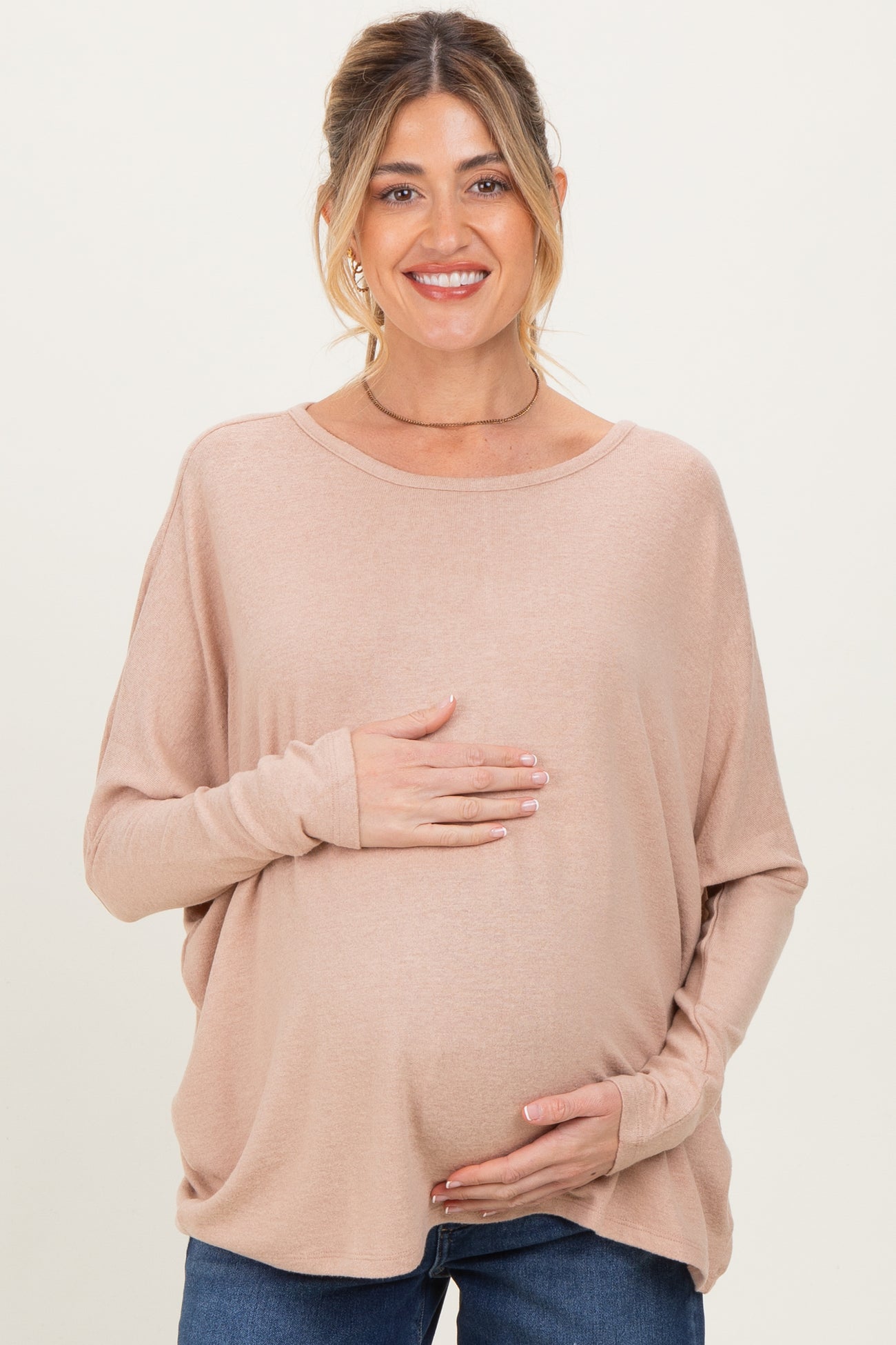 woman wearing a light pink maternity top and holding her baby bump while smiling