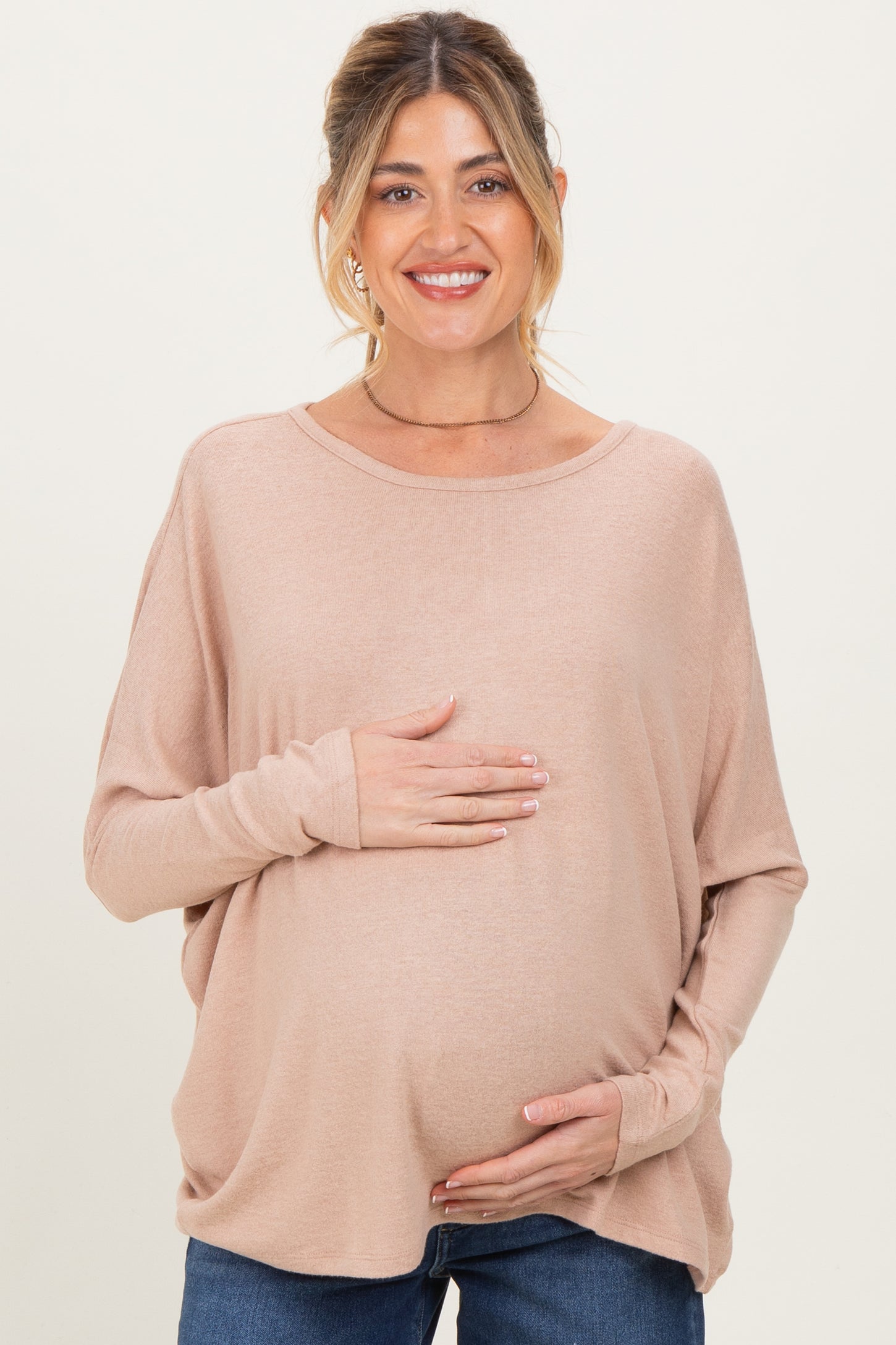 woman wearing a light pink maternity top and holding her baby bump while smiling
