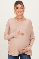 woman wearing a light pink maternity top and holding her baby bump while smiling