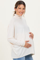 woman wearing a cream maternity turtleneck sweater and gently cradling her baby bump