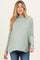 woman wearing a light green maternity top with a cowl neckline and long sleeves, paired with dark denim jeans