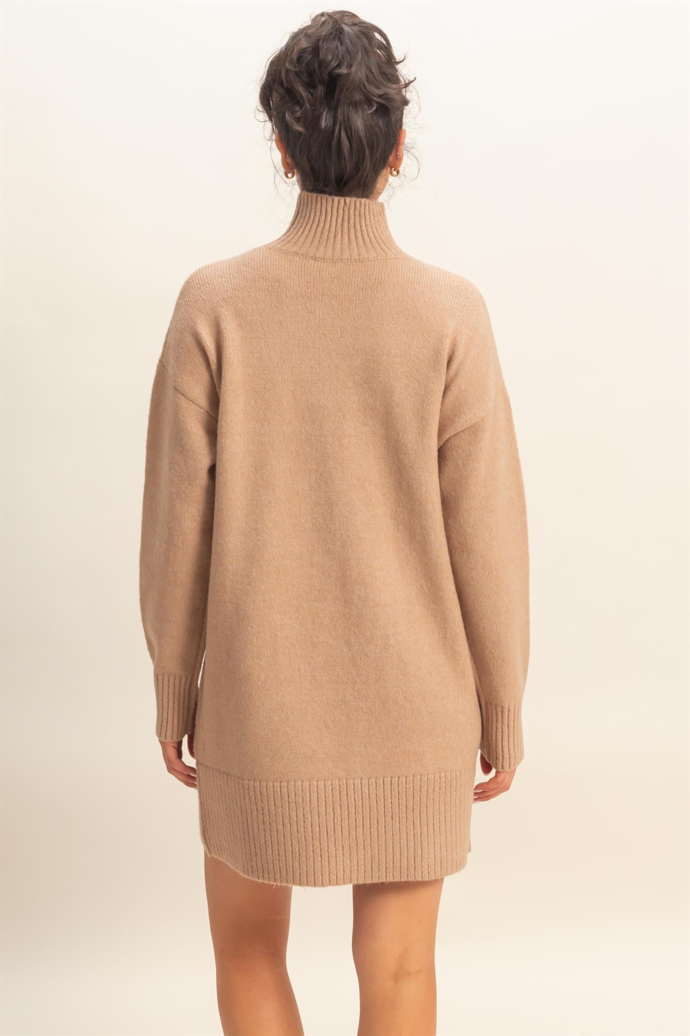woman wearing a cozy beige oversized sweater dress with a high neckline and ribbed hem, seen from the back