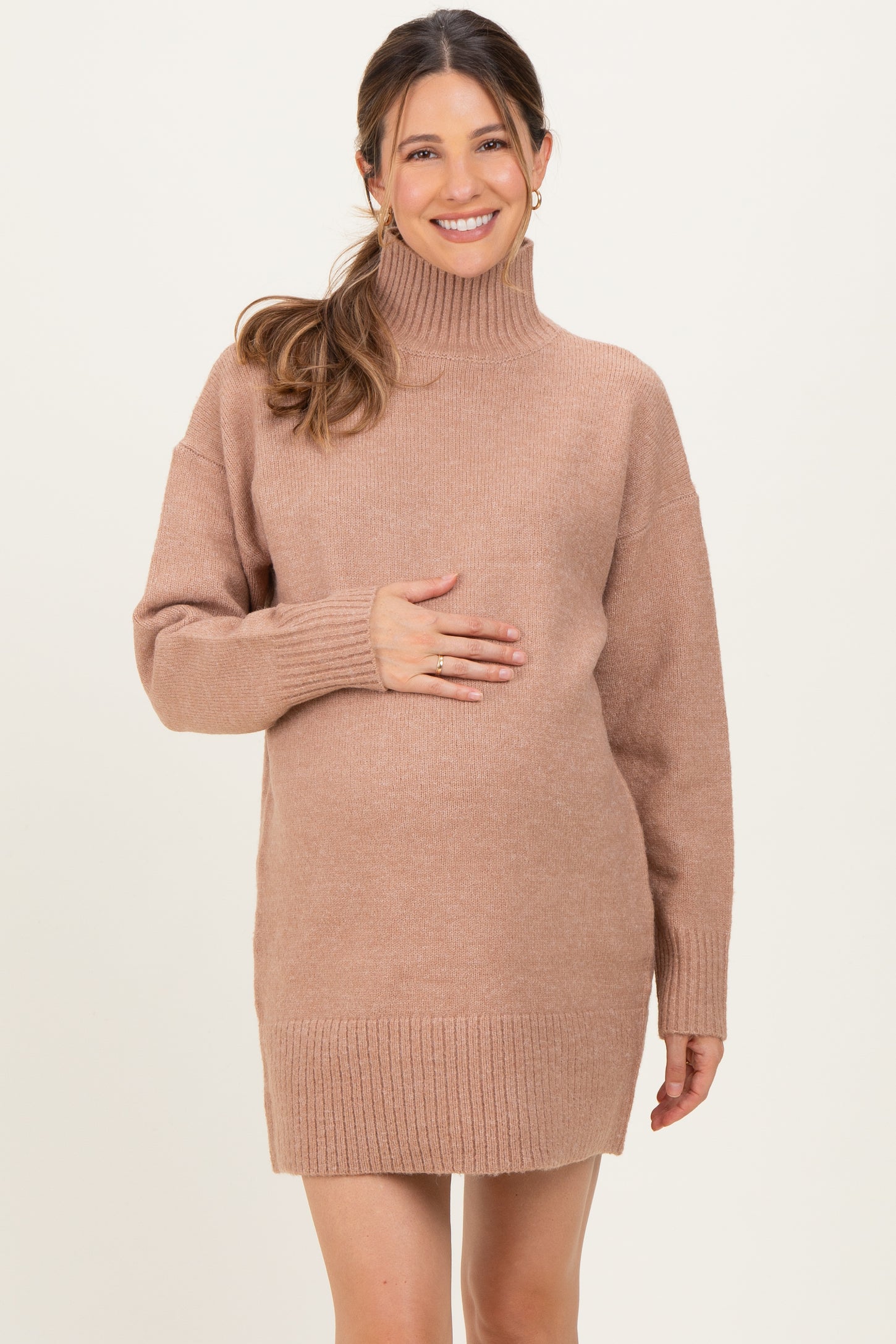 woman wearing a brown oversized maternity sweater dress and holding her baby bump