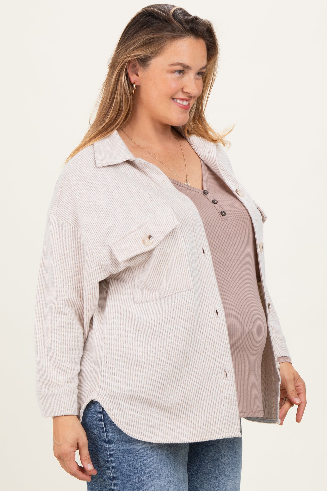 woman wearing a beige ribbed button-up shirt over a brown maternity tank top, showing her baby bump