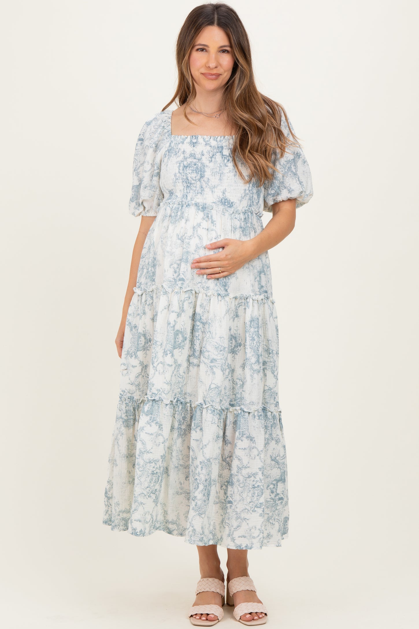 woman wearing a blue and white floral print maternity maxi dress and holding her baby bump