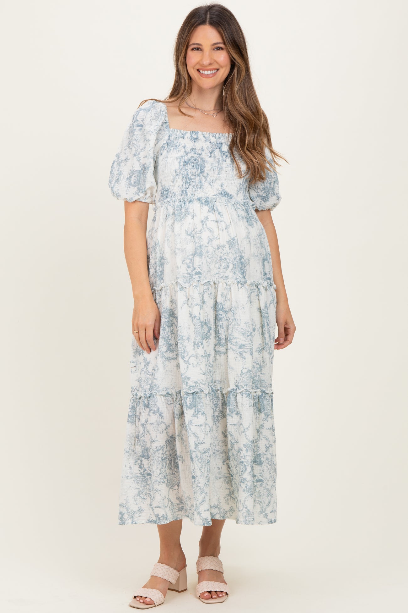 woman wearing a blue and white floral print maternity maxi dress with puff sleeves and a smocked bodice, smiling