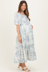 woman wearing a blue and white floral print maternity maxi dress with puff sleeves and a visible baby bump
