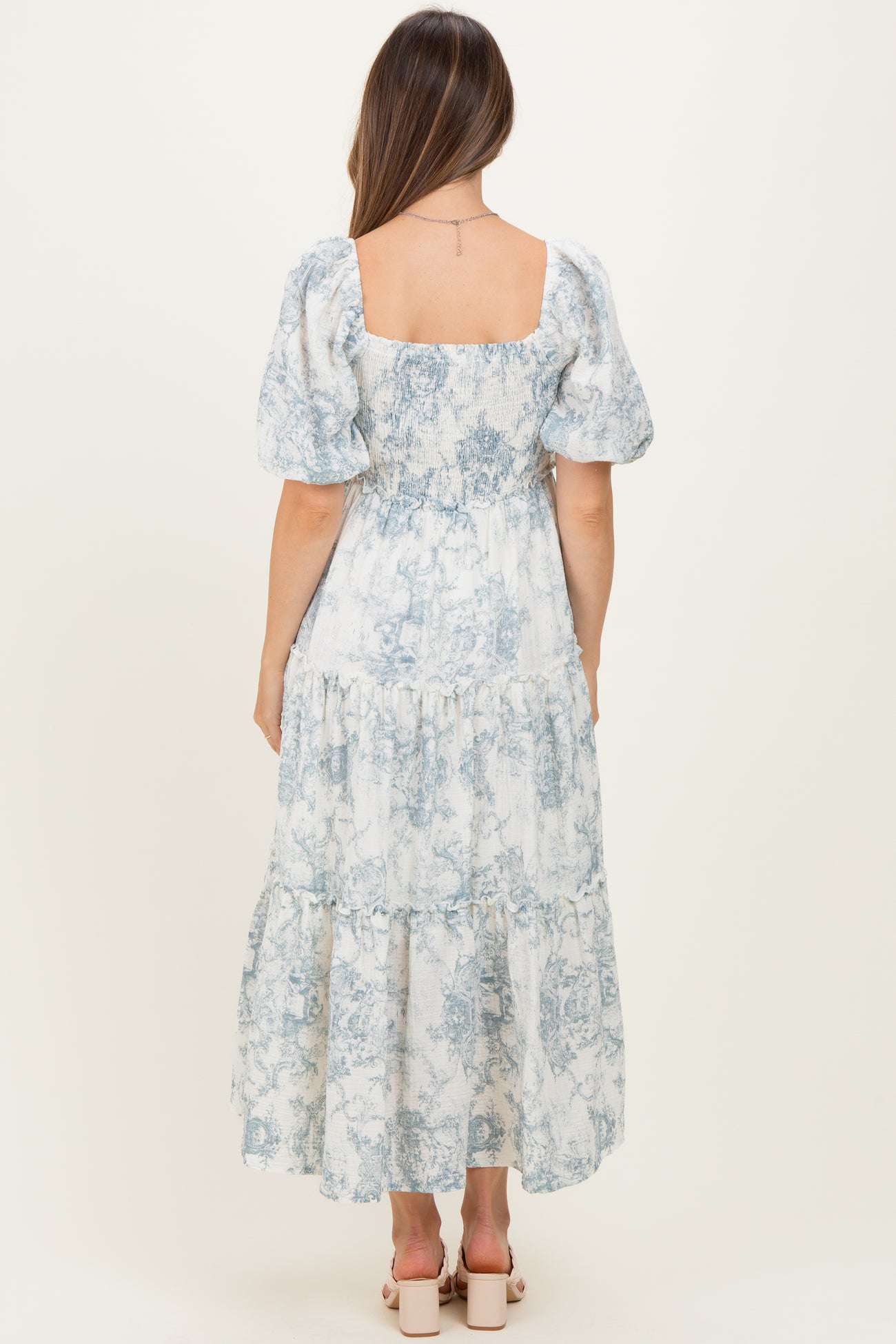 woman wearing a blue and white patterned maternity maxi dress with puff sleeves and a tiered skirt, showing her baby bump