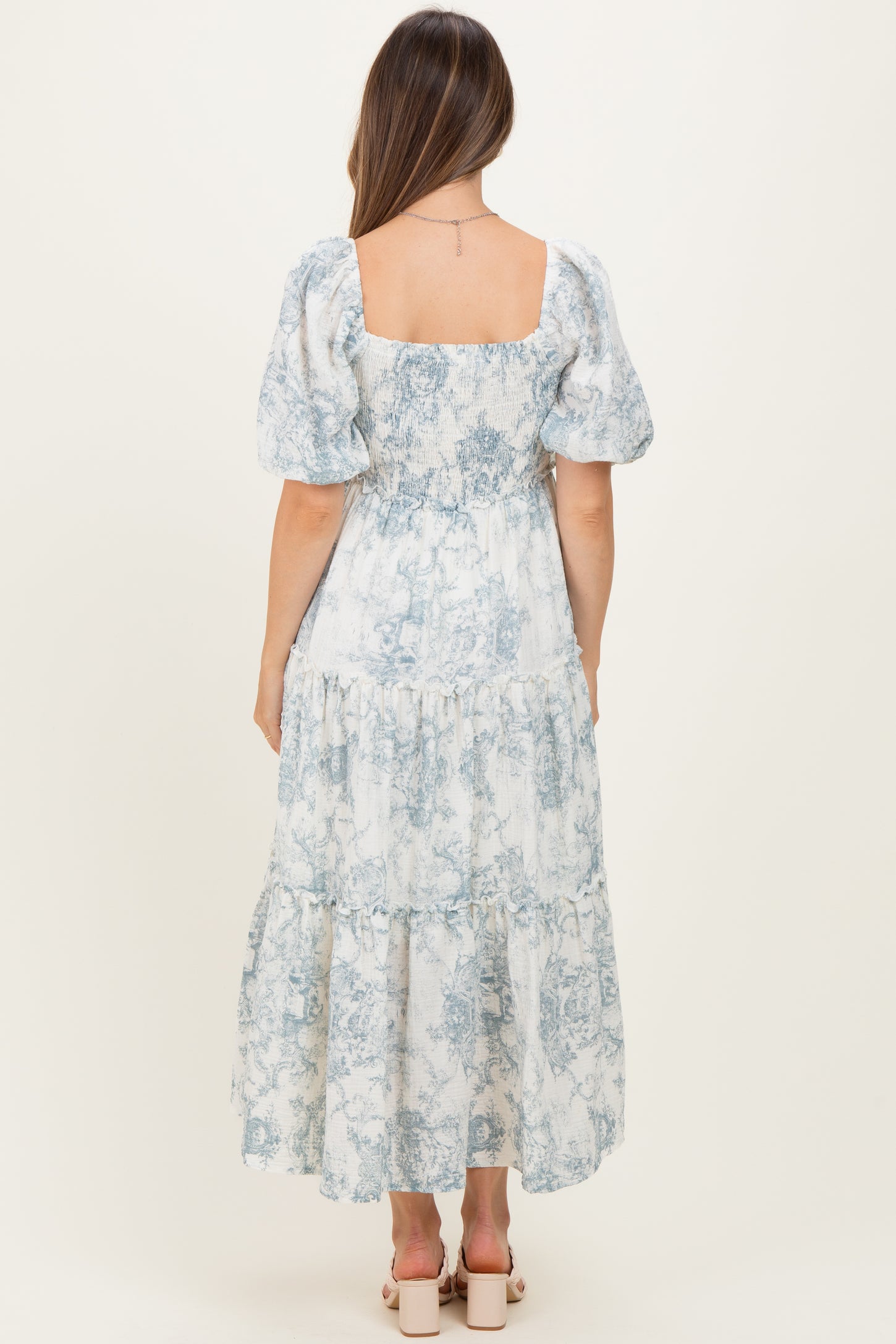 woman wearing a blue and white patterned maternity maxi dress with puff sleeves and a tiered skirt, showing her baby bump