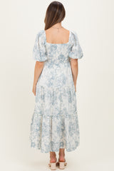 woman wearing a blue and white patterned maternity maxi dress with puff sleeves and a tiered skirt, showing her baby bump
