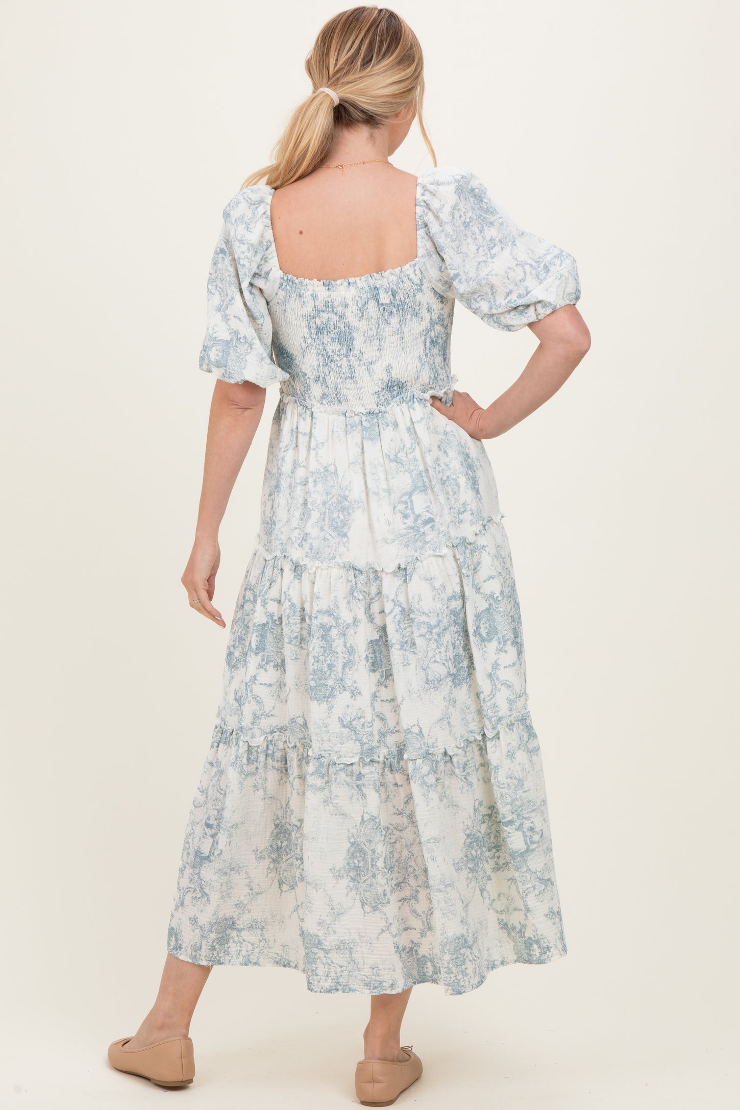 woman wearing a back view of a blue and white floral maxi dress with puff sleeves and tiered skirt