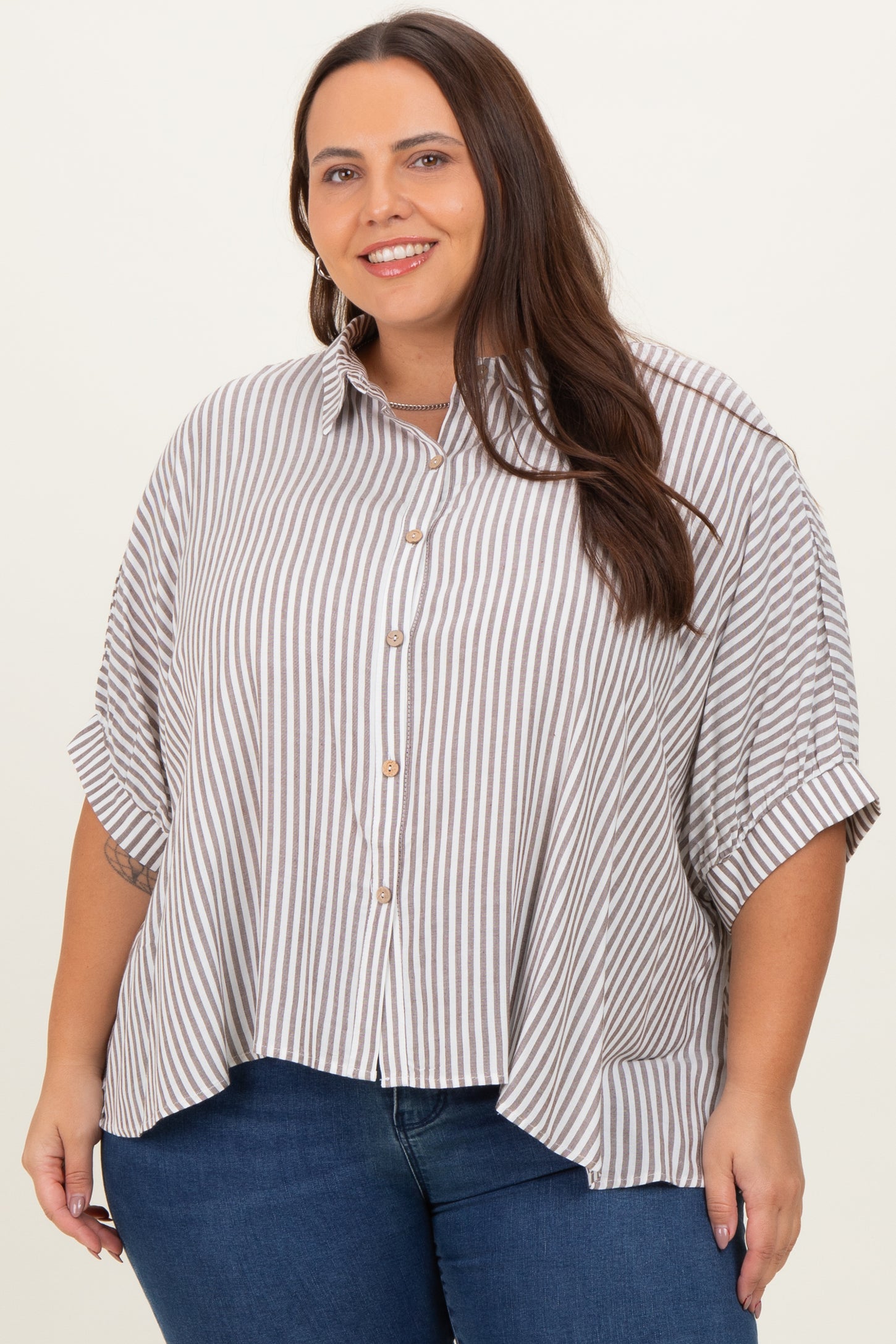 woman wearing a beige and white striped plus size button-up shirt with rolled sleeves and high-low hem