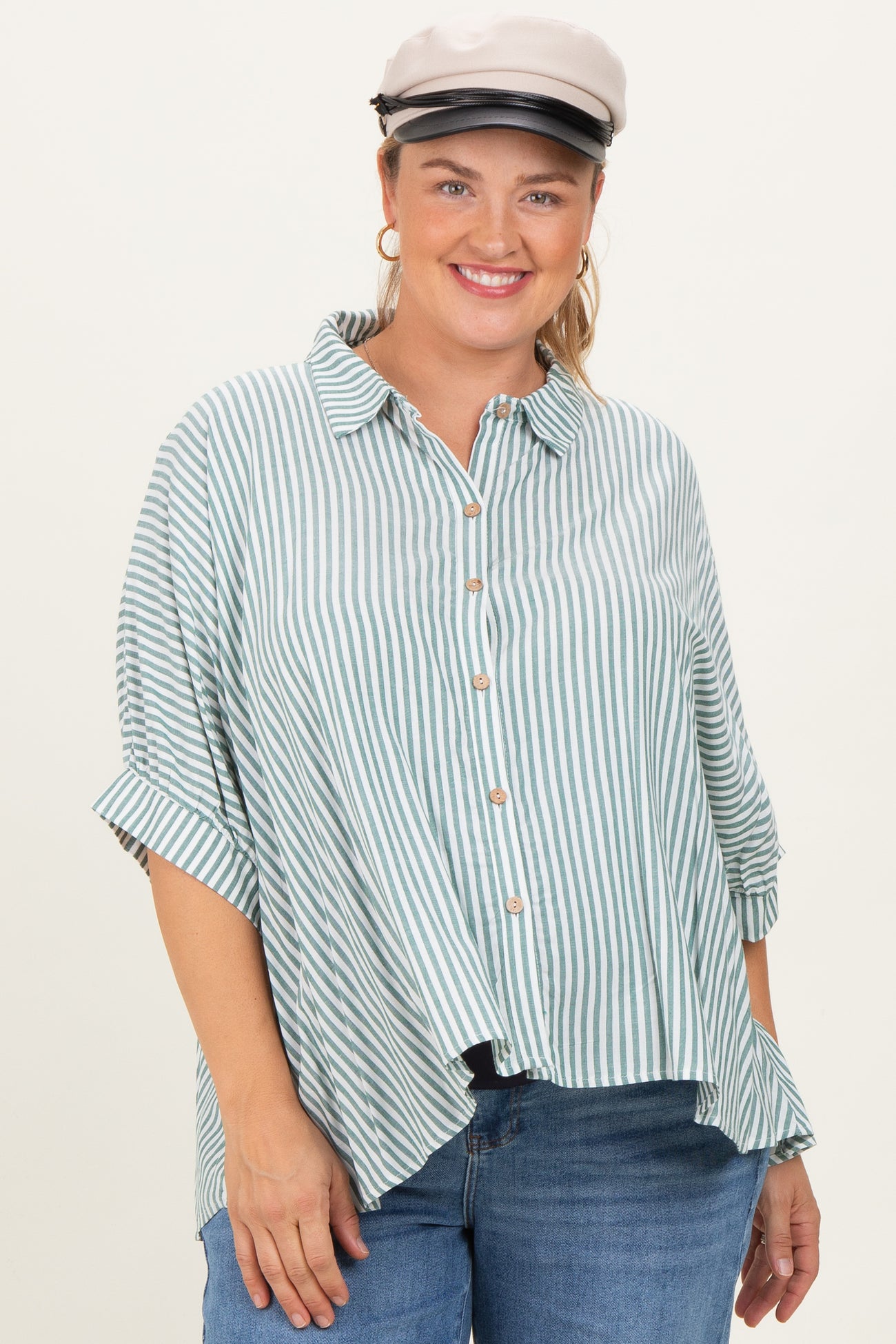 woman wearing a green and white striped maternity plus button-up shirt with rolled sleeves and a playful smile