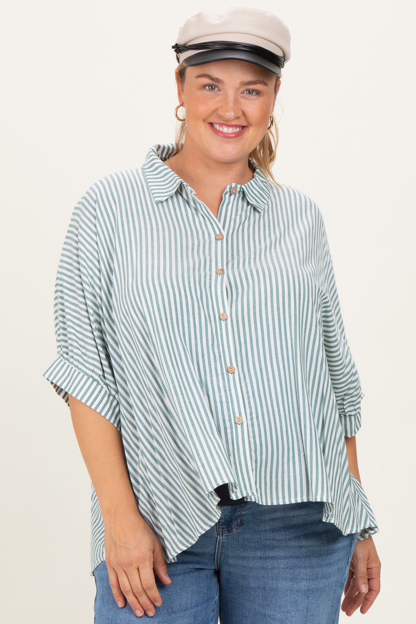 woman wearing a green and white striped maternity plus button-up shirt with rolled sleeves and a playful smile
